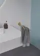 Handtuchstange aus gebürstetem Gold von Ideal Standard, an der Wand montiert, mit einem grauen Handtuch, daneben ein Behälter und Zahnbürste auf einer weißen Ablage.